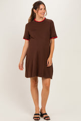 woman wearing a brown maternity dress with a red ruffled collar and sleeves, standing and showing her baby bump