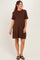 woman wearing a brown maternity dress with a red ruffled collar and sleeves, standing and showing her baby bump