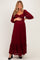 woman wearing a burgundy lace maternity maxi dress with puff sleeves and a ruffled hem, holding her baby bump