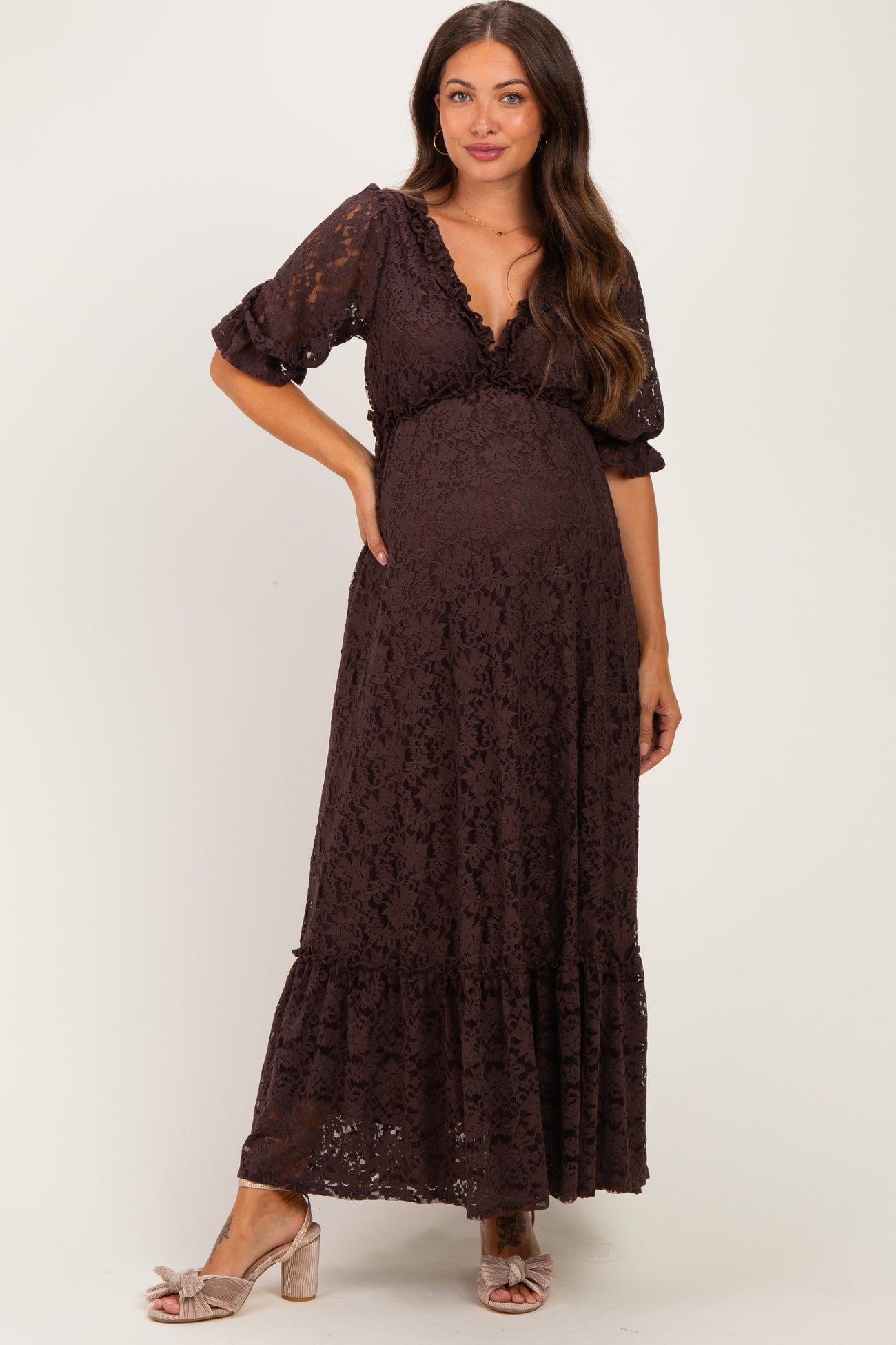 woman wearing a dark brown lace maternity maxi dress with a plunging neckline and short puff sleeves, showing her baby bump
