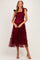 woman wearing a burgundy maternity dress with ruffle straps and tiered tulle skirt, highlighting her baby bump