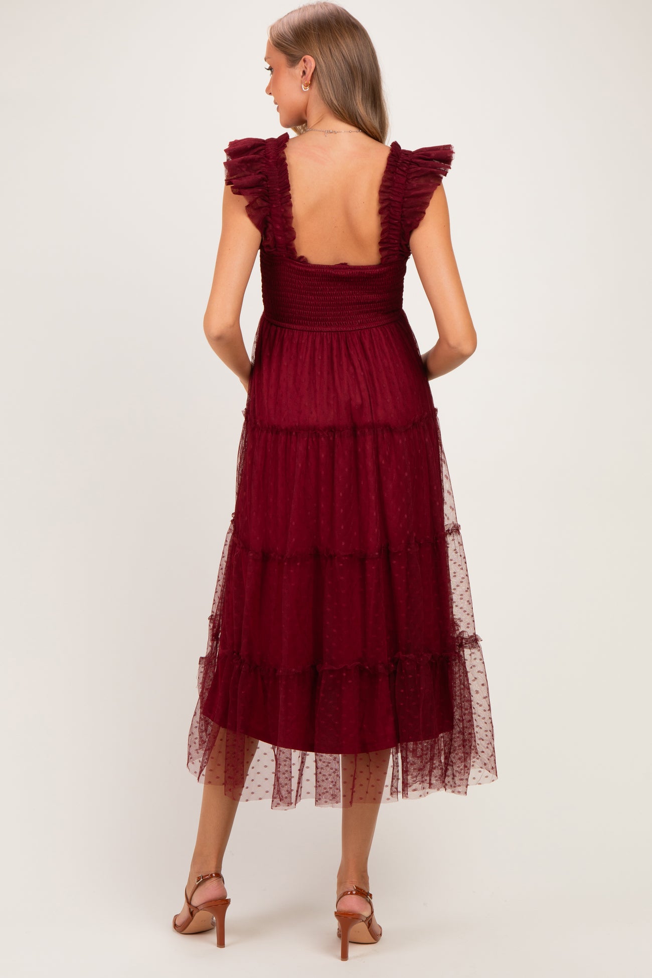 woman wearing a burgundy maternity dress with ruffled straps and tiered tulle details, showing the back view