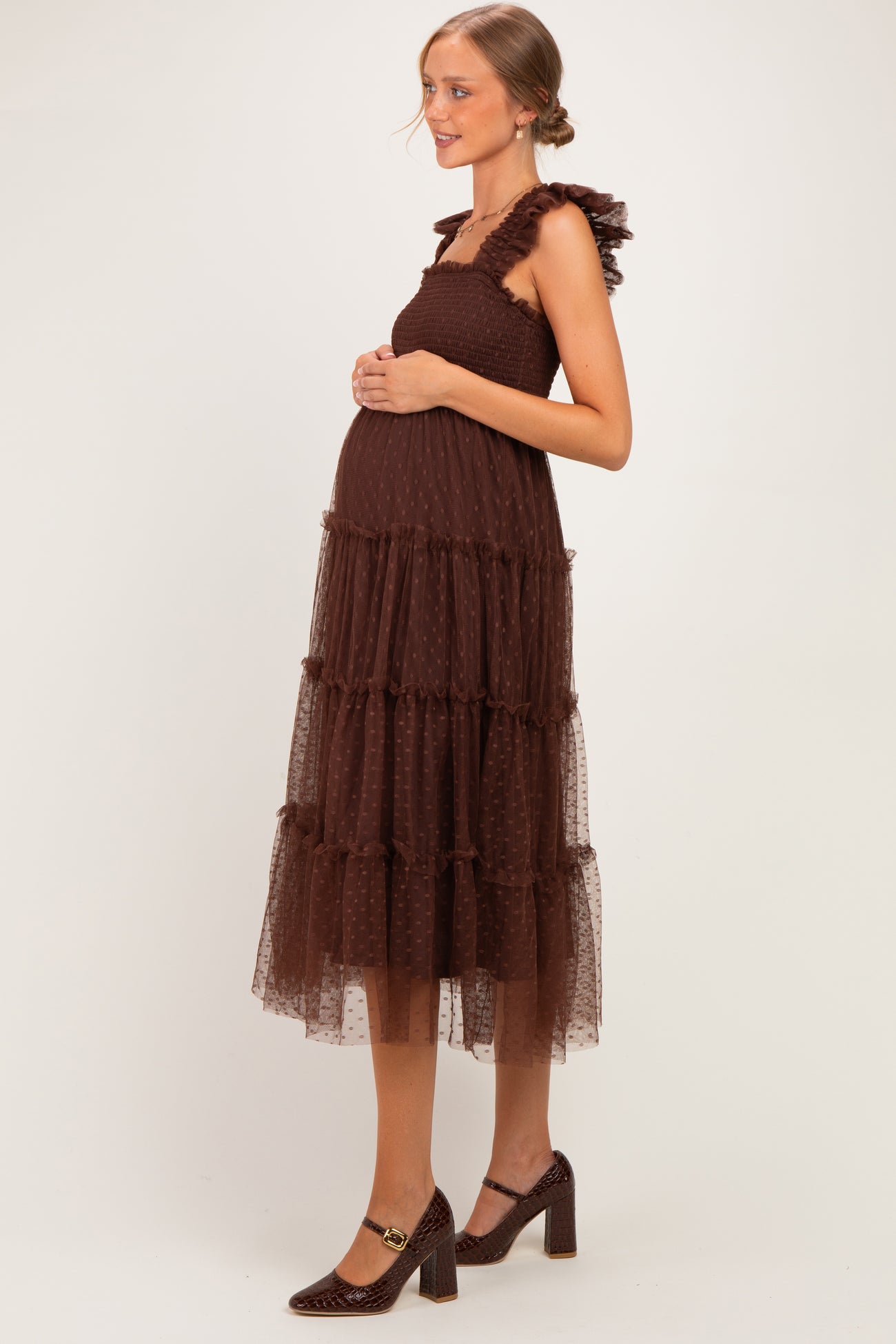 woman wearing a brown maternity dress with ruffled straps and a tiered tulle design, showcasing a baby bump