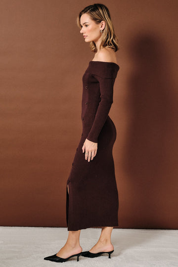 woman wearing a burgundy off-shoulder ribbed midi dress with buttons and thigh slit, styled with black heels