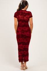 woman wearing a burgundy floral maternity dress with a lace hem and short sleeves, standing with her back to the camera