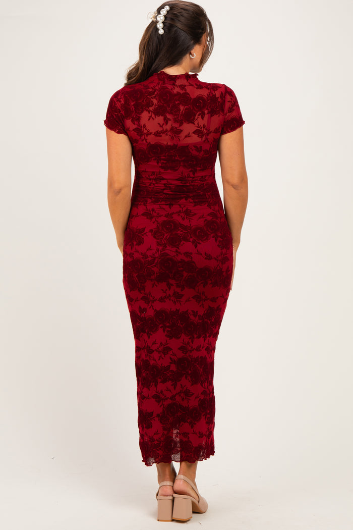 woman wearing a burgundy floral maternity dress with a lace hem and short sleeves, standing with her back to the camera