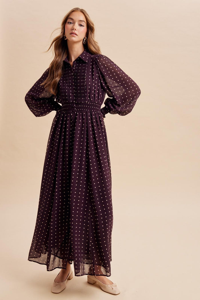 woman wearing a long burgundy polka dot maxi dress with a smocked waist and puff sleeves