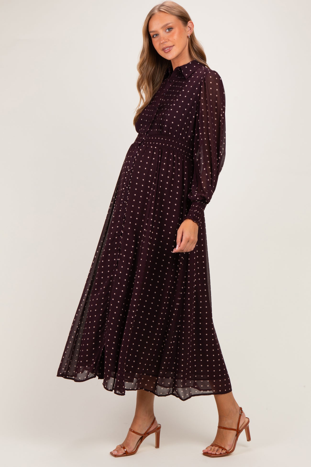 woman wearing a burgundy maternity dress with white polka dots and long sleeves, showcasing her baby bump