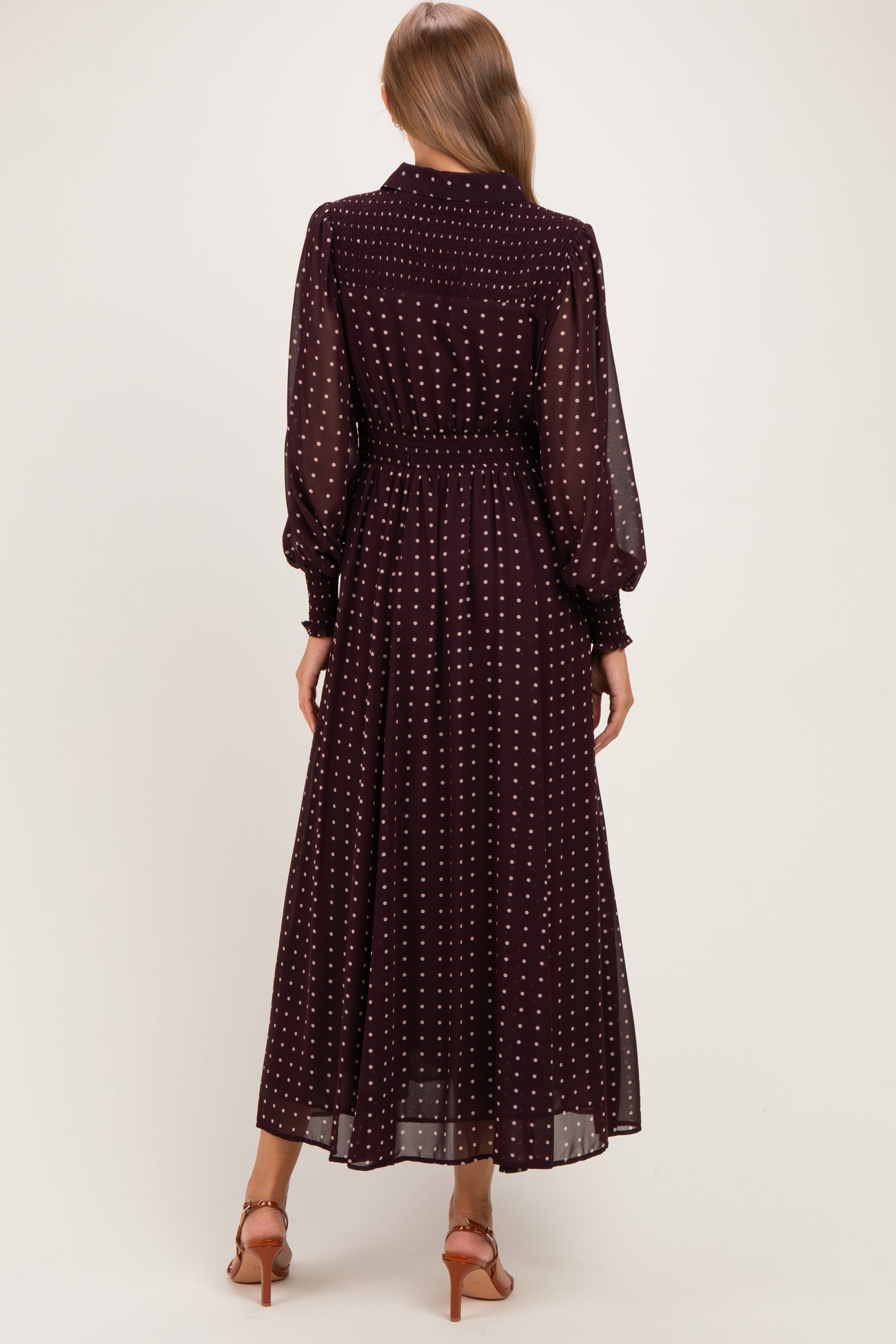 woman wearing a burgundy long sleeve maternity dress with white polka dots, showing the back view and a flowing skirt
