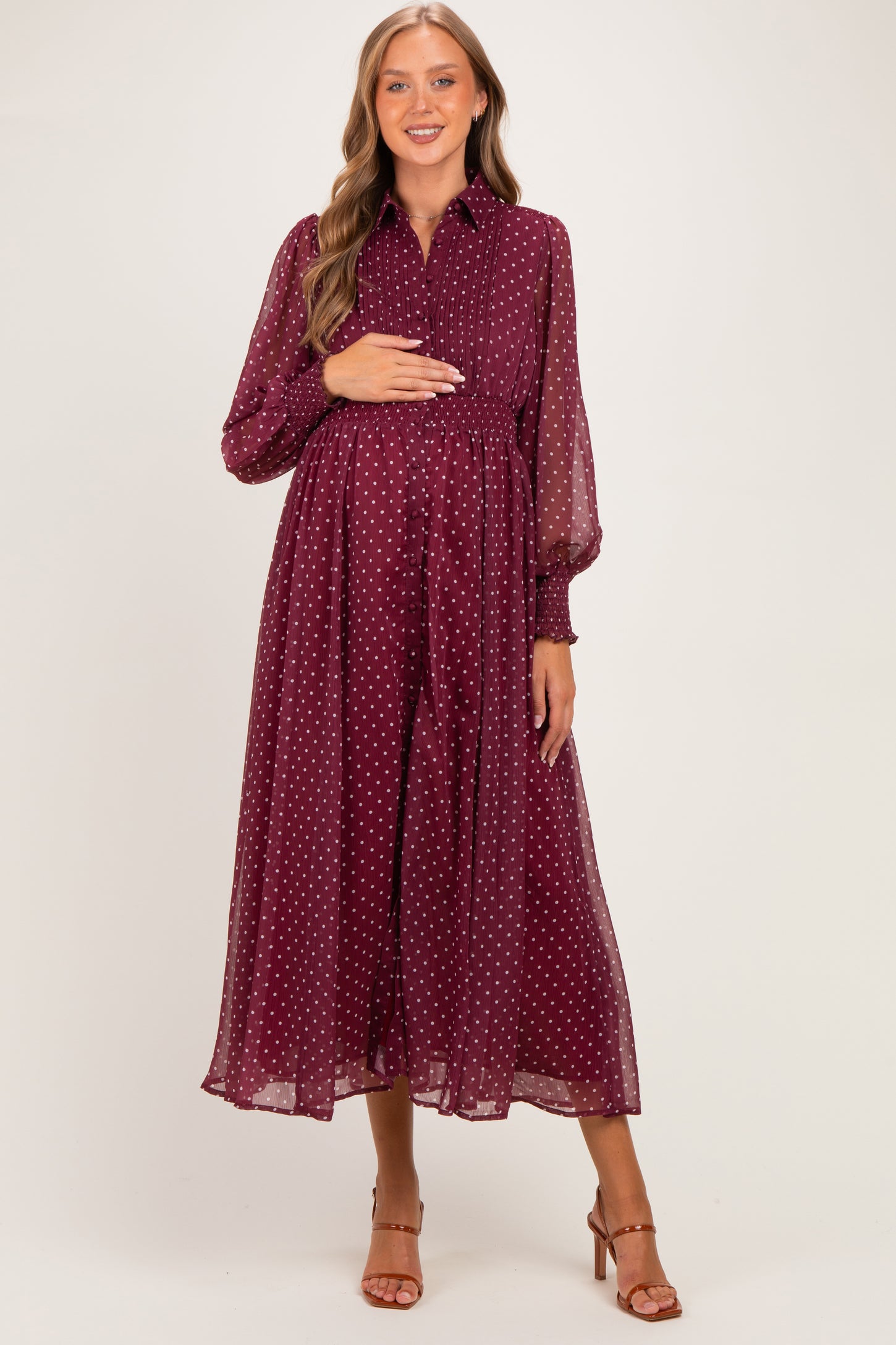 woman wearing a burgundy polka dot maternity dress with long sleeves and a cinched waist, holding her baby bump