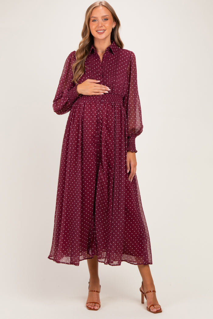 woman wearing a burgundy polka dot maternity dress with long sleeves and a cinched waist, holding her baby bump