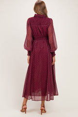 woman wearing a burgundy polka dot maternity dress with long sheer sleeves and a cinched waist, view from the back