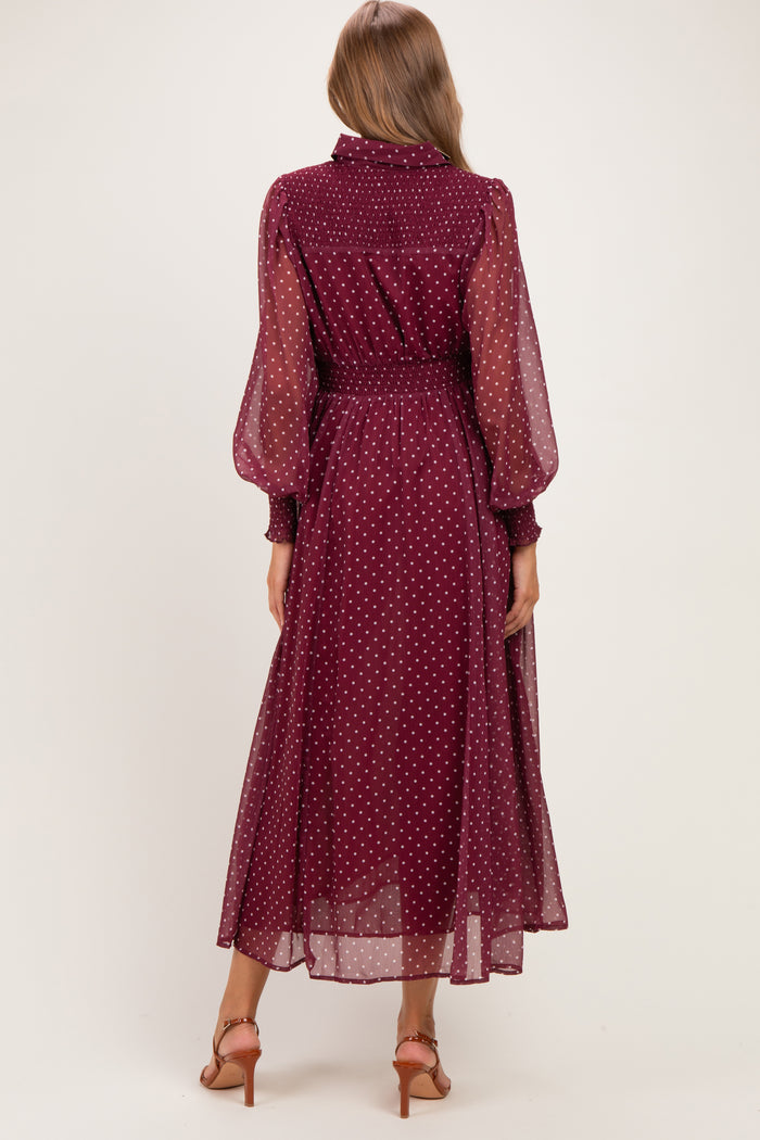 woman wearing a burgundy polka dot maternity dress with long sheer sleeves and a cinched waist, view from the back