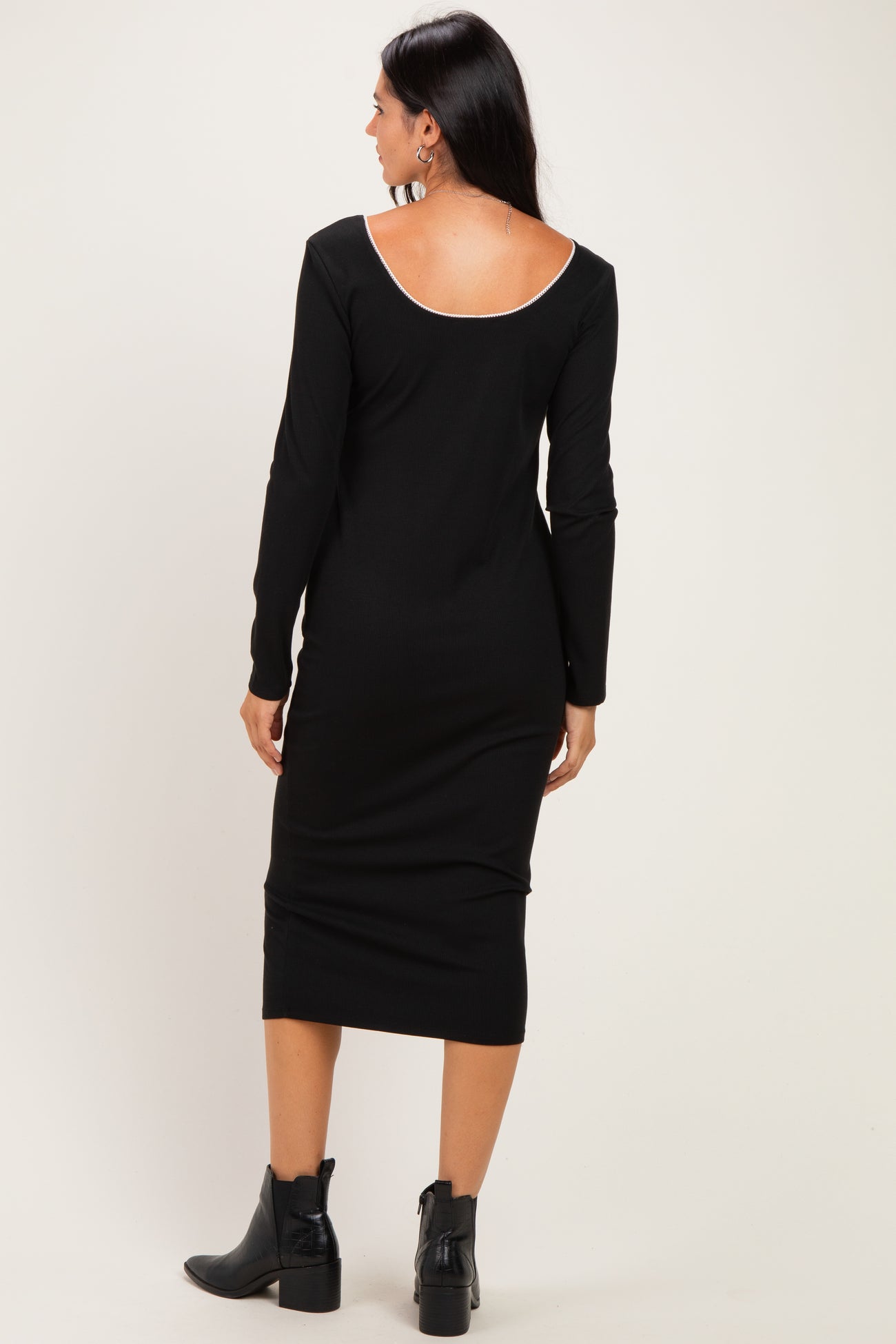 woman wearing a black long sleeve fitted midi dress with a low back and side slit, paired with black ankle boots