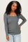 woman wearing a gray long sleeve top with a square neckline and a decorative detail, paired with light blue jeans