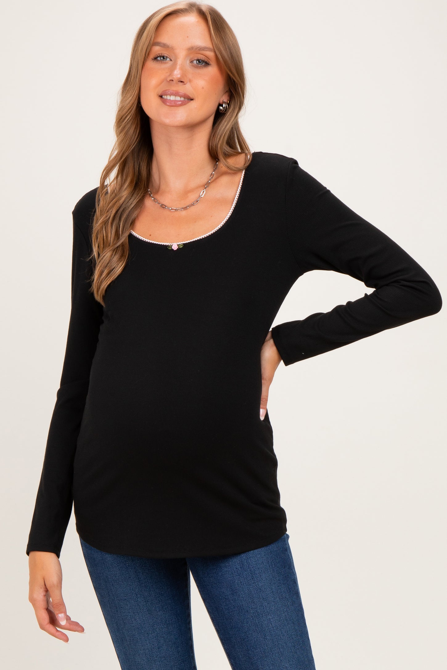 woman wearing a black long sleeve maternity top with a scoop neckline and a slight shimmer trim, showing her baby bump