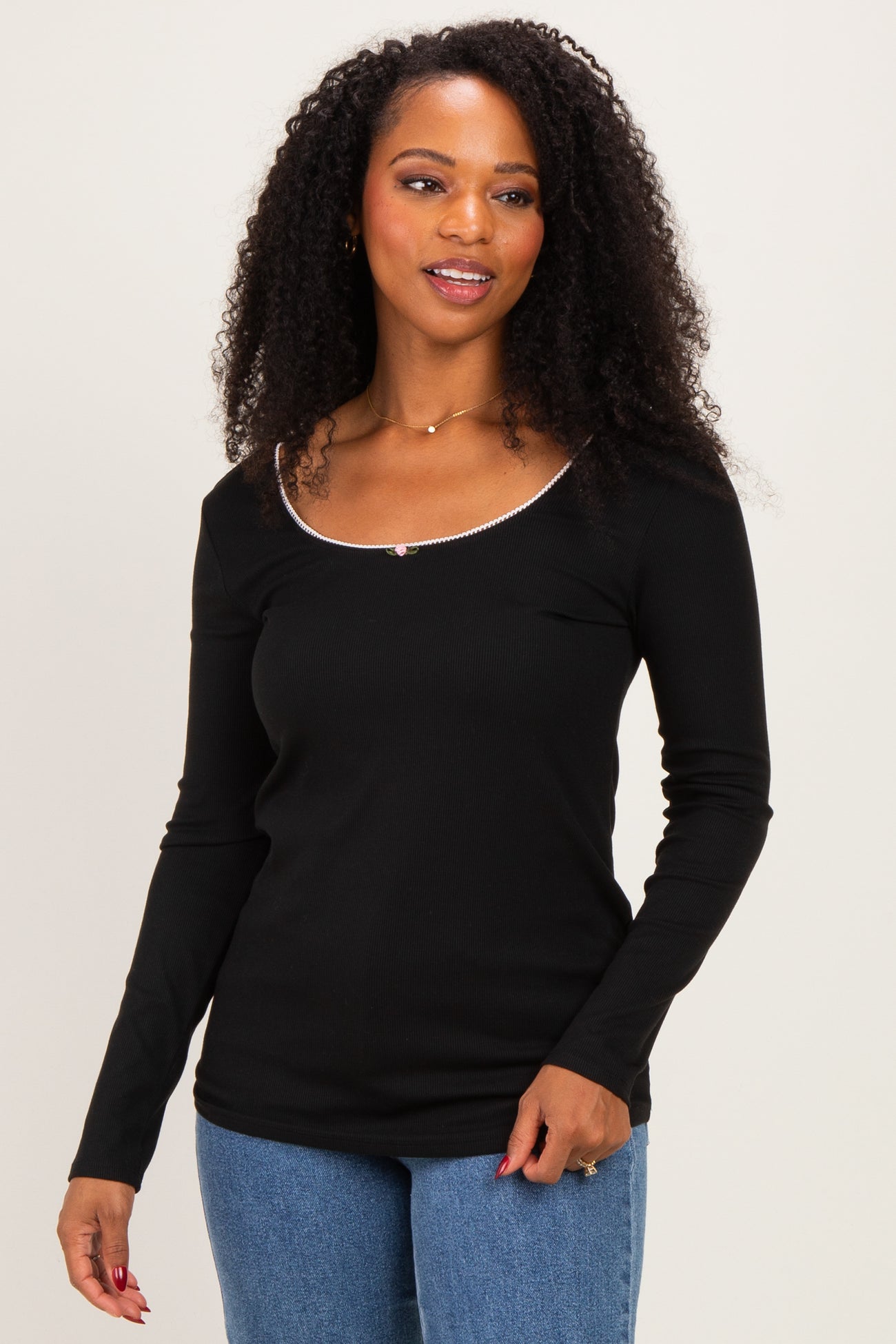 woman wearing a black long sleeve top with a scoop neckline and a decorative trim, styled with blue jeans