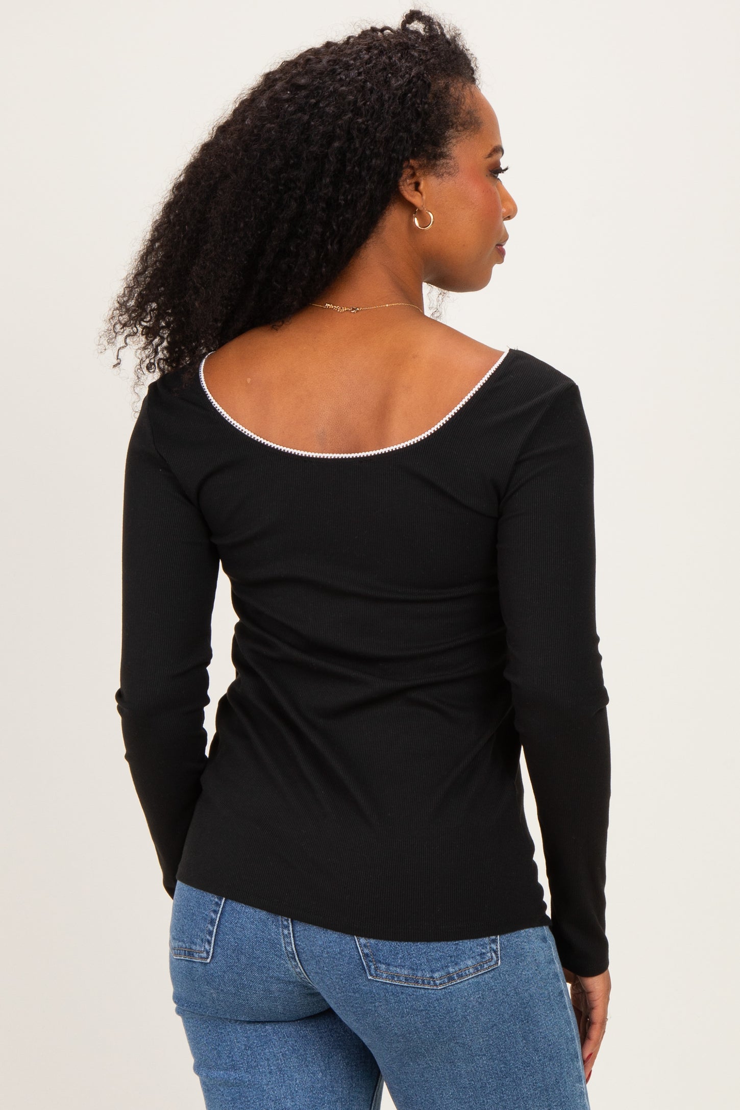 woman wearing a black long sleeve top with a scoop back and ribbed texture, paired with blue jeans