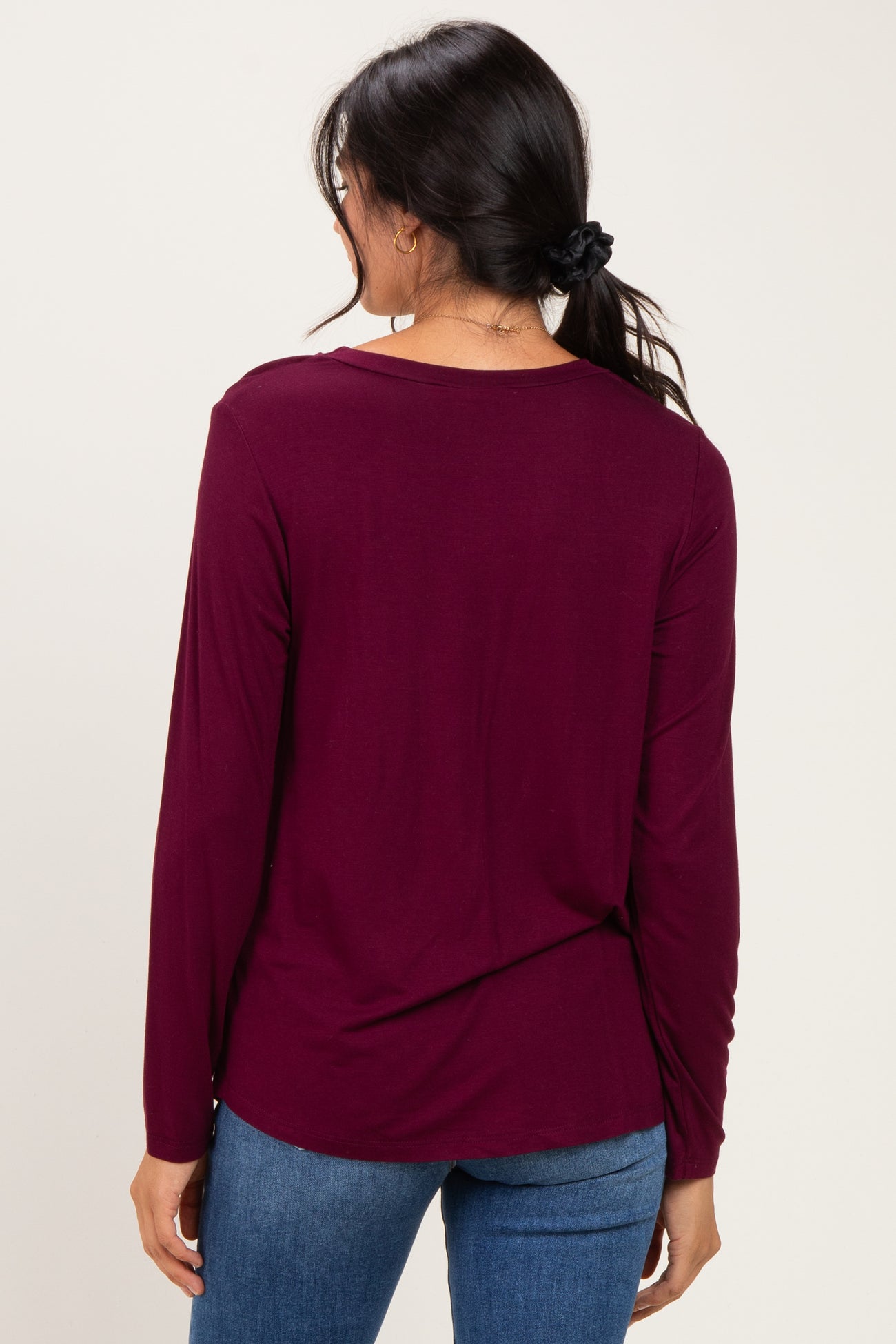 woman wearing a burgundy long sleeve top, viewed from the back, paired with blue jeans