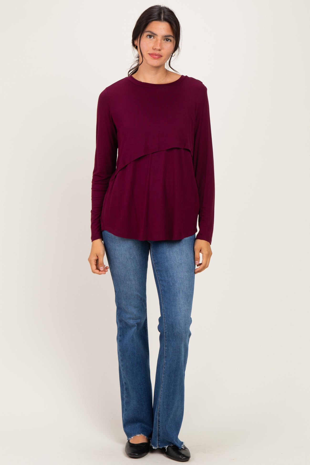 woman wearing a burgundy long sleeve top with a layered design paired with light blue flared jeans