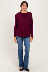 woman wearing a burgundy long sleeve top with a layered design paired with light blue flared jeans