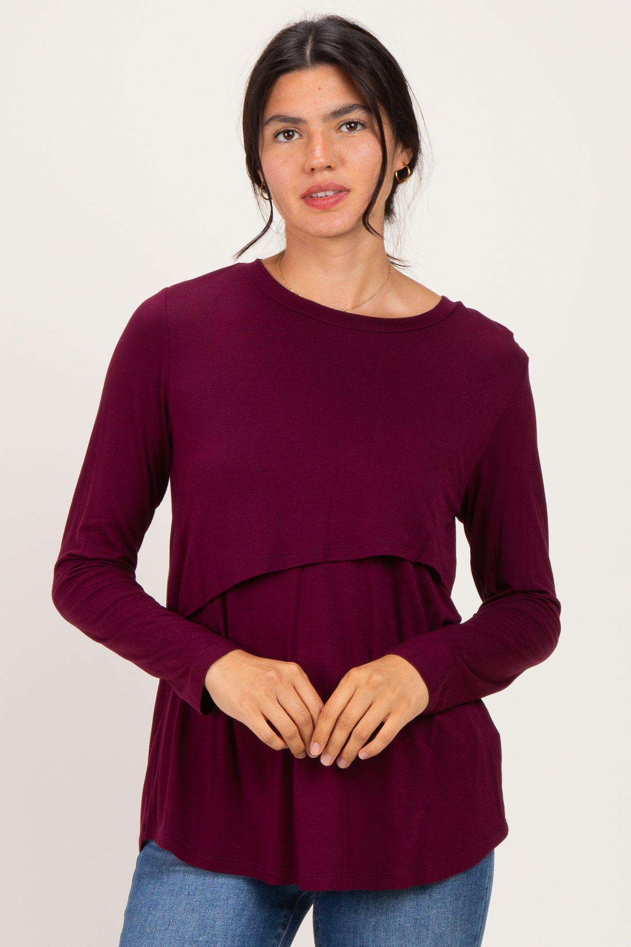 woman wearing a burgundy long sleeve top with a layered design and relaxed fit, posing against a plain background