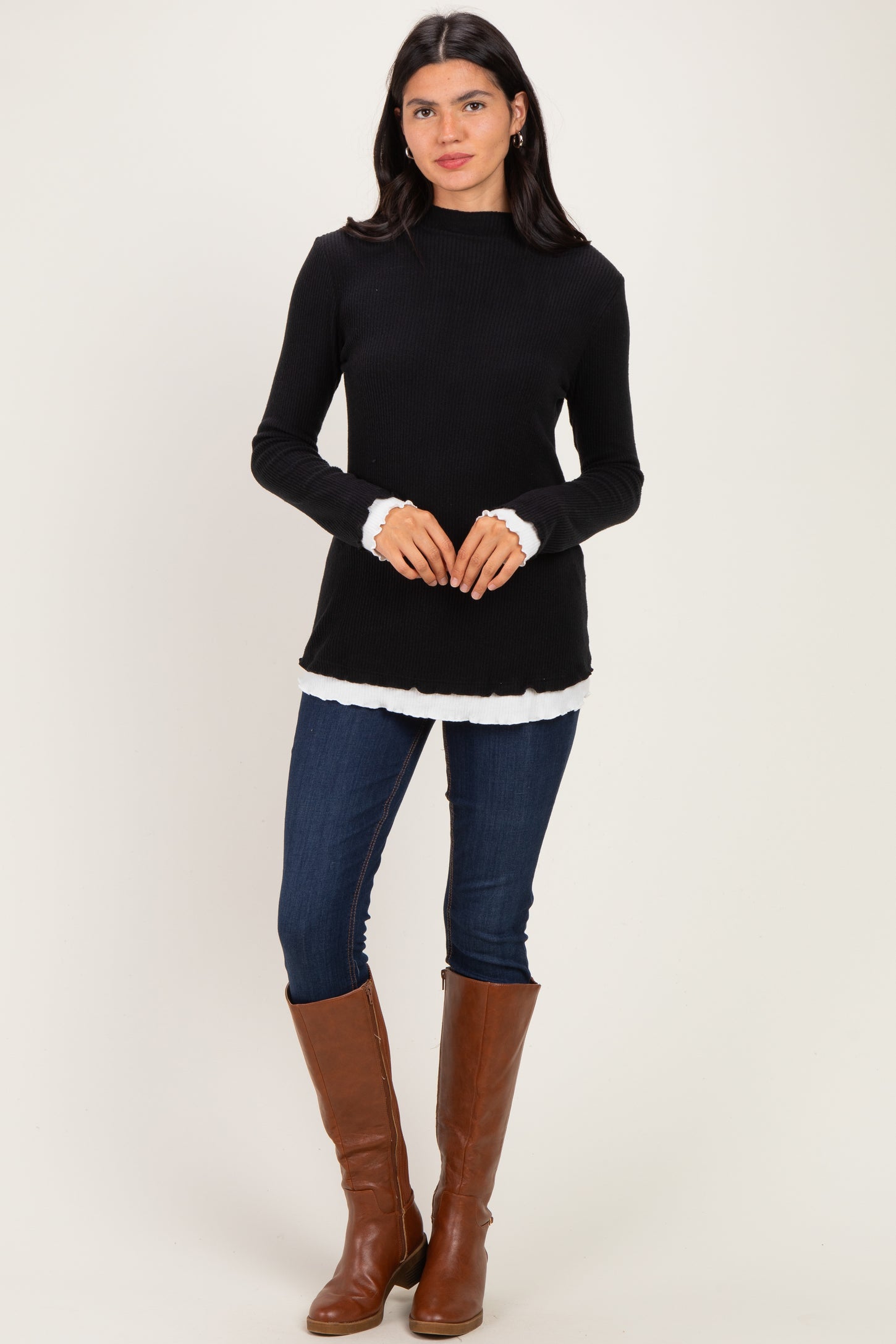 woman wearing a black ribbed long sleeve top with ruffled hem and cuffs, paired with skinny jeans and brown knee-high boots