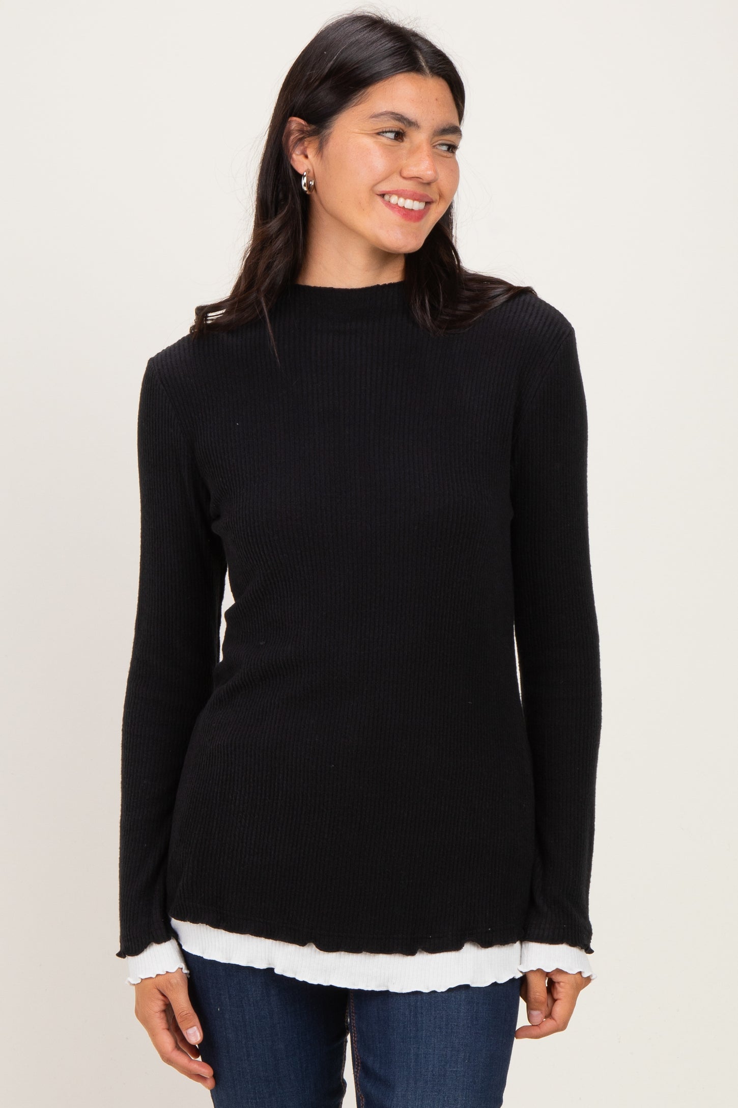 woman wearing a black ribbed long sleeve top with a white layered hem and smiling