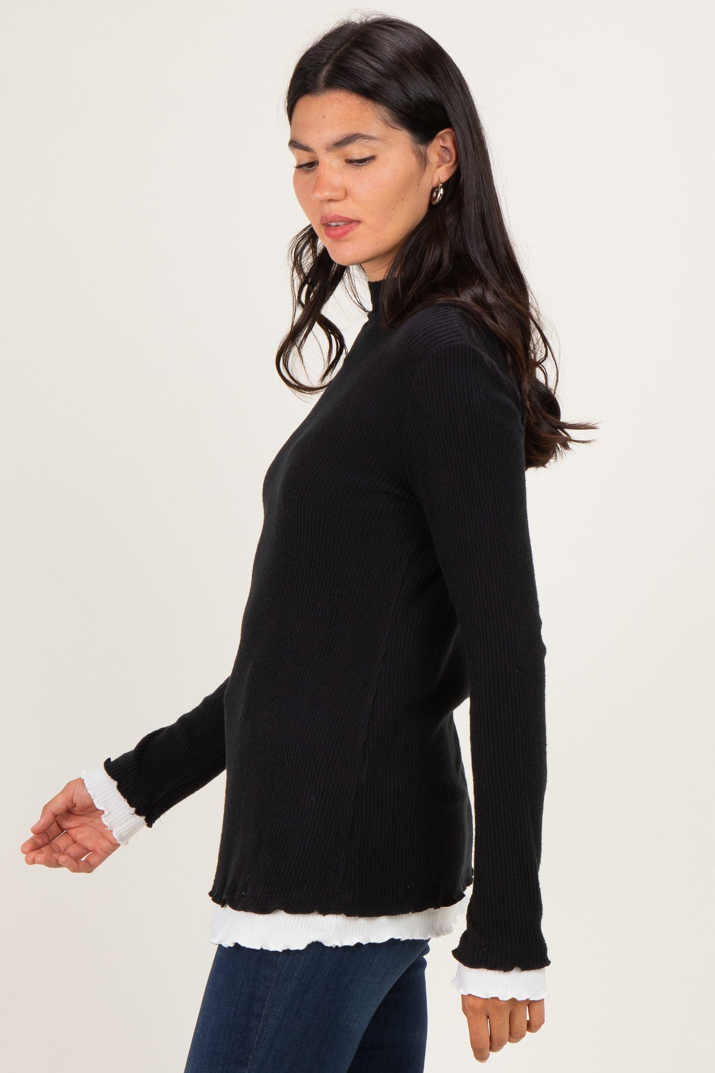 woman wearing a black ribbed long sleeve top with white ruffle details on the cuffs and hem
