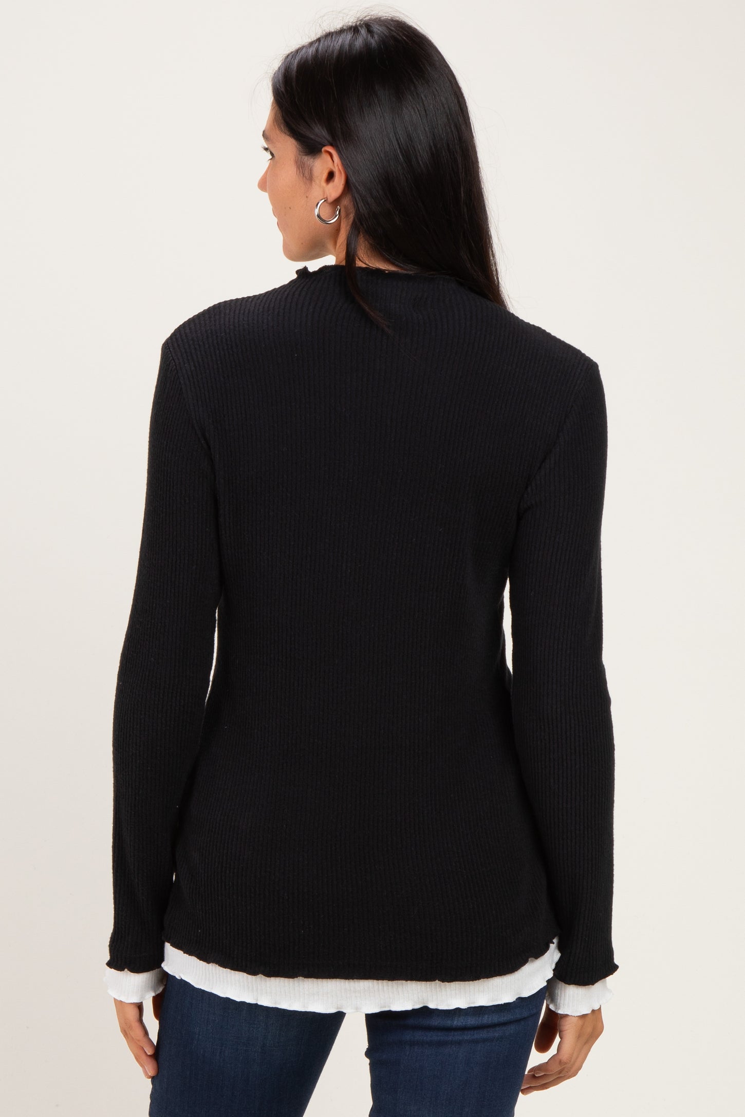 woman wearing a black ribbed long sleeve top with a white layered hem, seen from the back