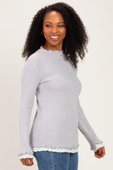 woman wearing a light gray ribbed long sleeve top with ruffled cuffs and hemline