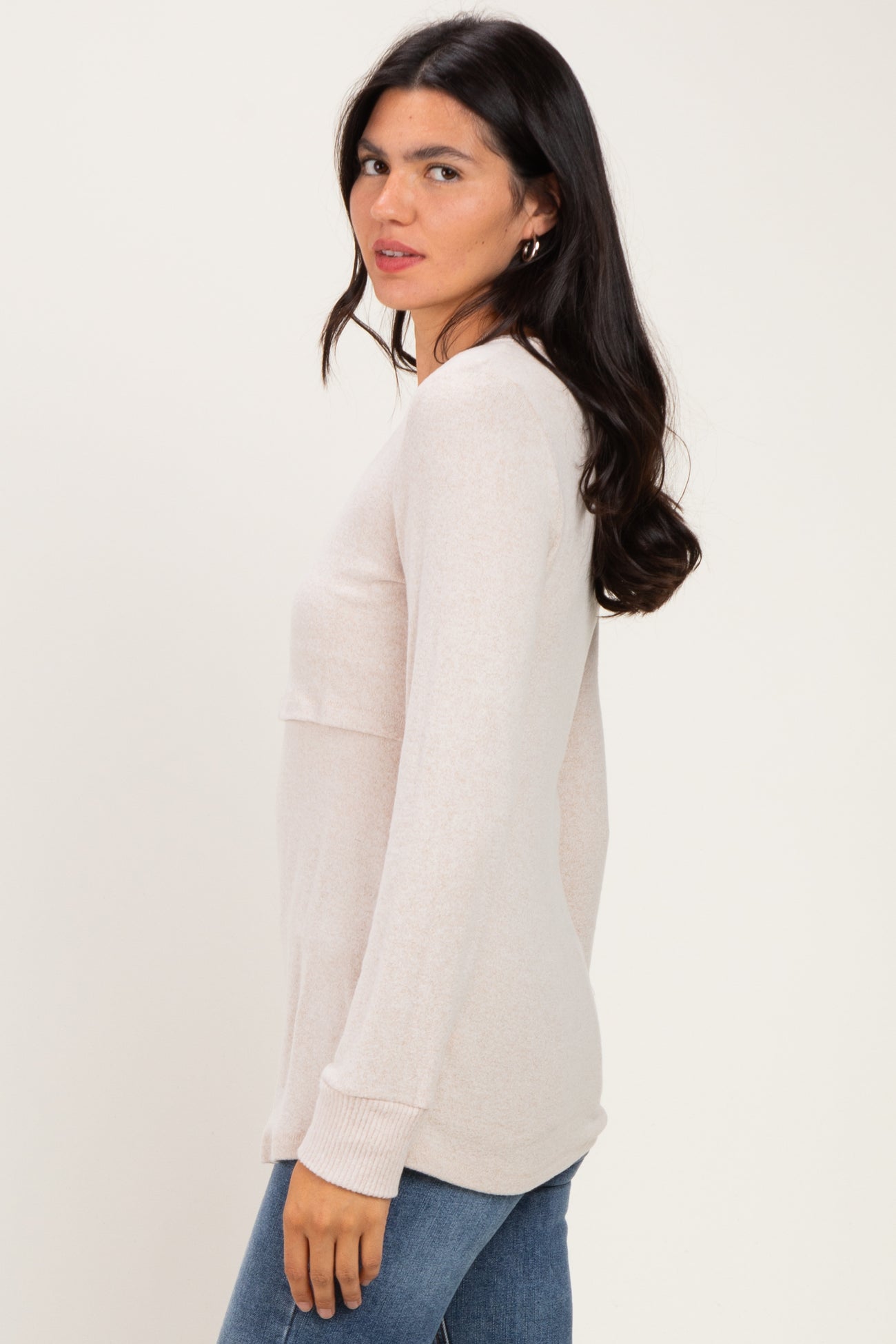 woman wearing a light pink long sleeve top with a relaxed fit and round neckline, styled with blue jeans
