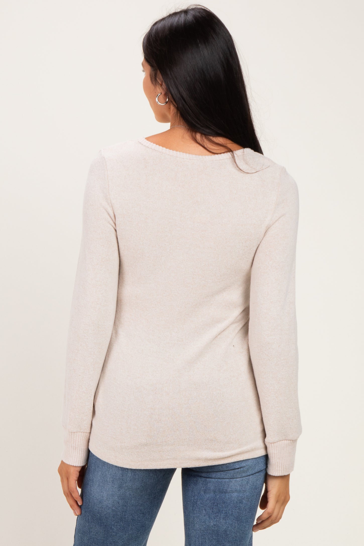 woman wearing a beige long sleeve sweater, shown from the back, paired with blue jeans