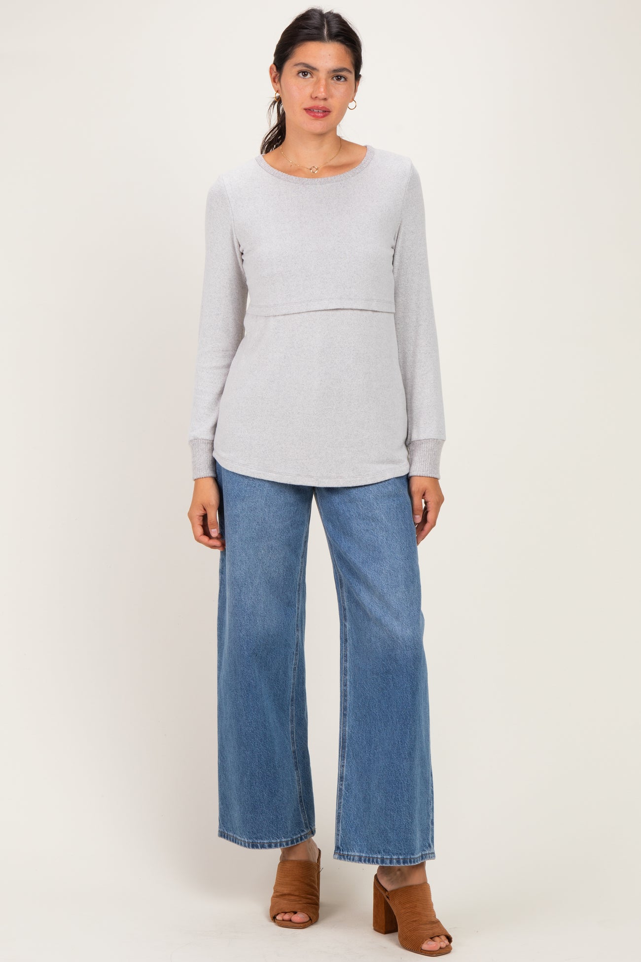 woman wearing a light gray long sleeve top with a gathered waist and wide-leg denim jeans