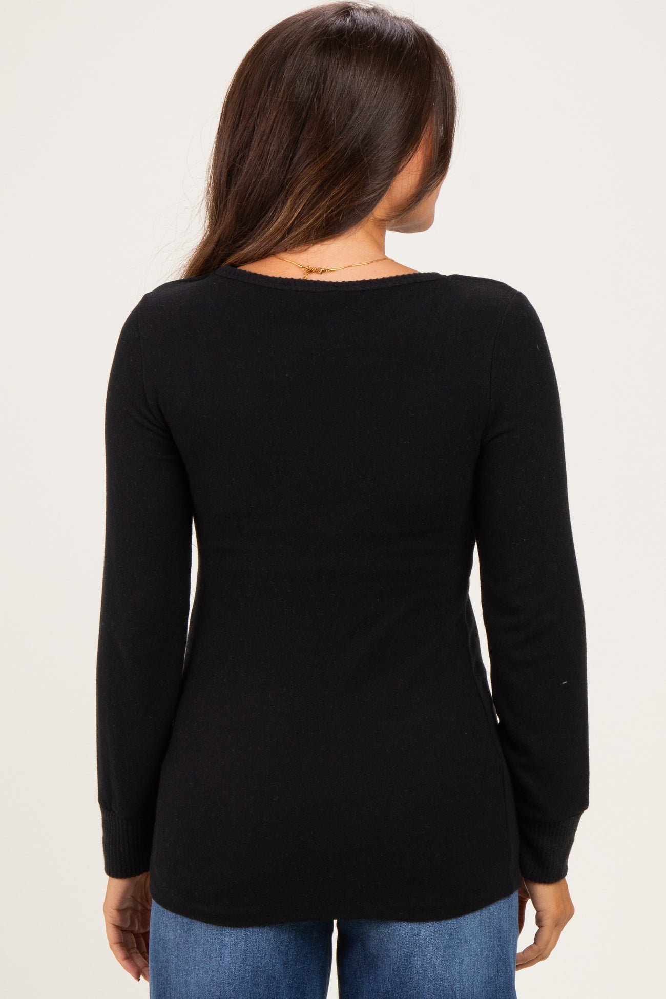woman wearing a black long sleeve maternity top, viewed from the back, paired with blue jeans