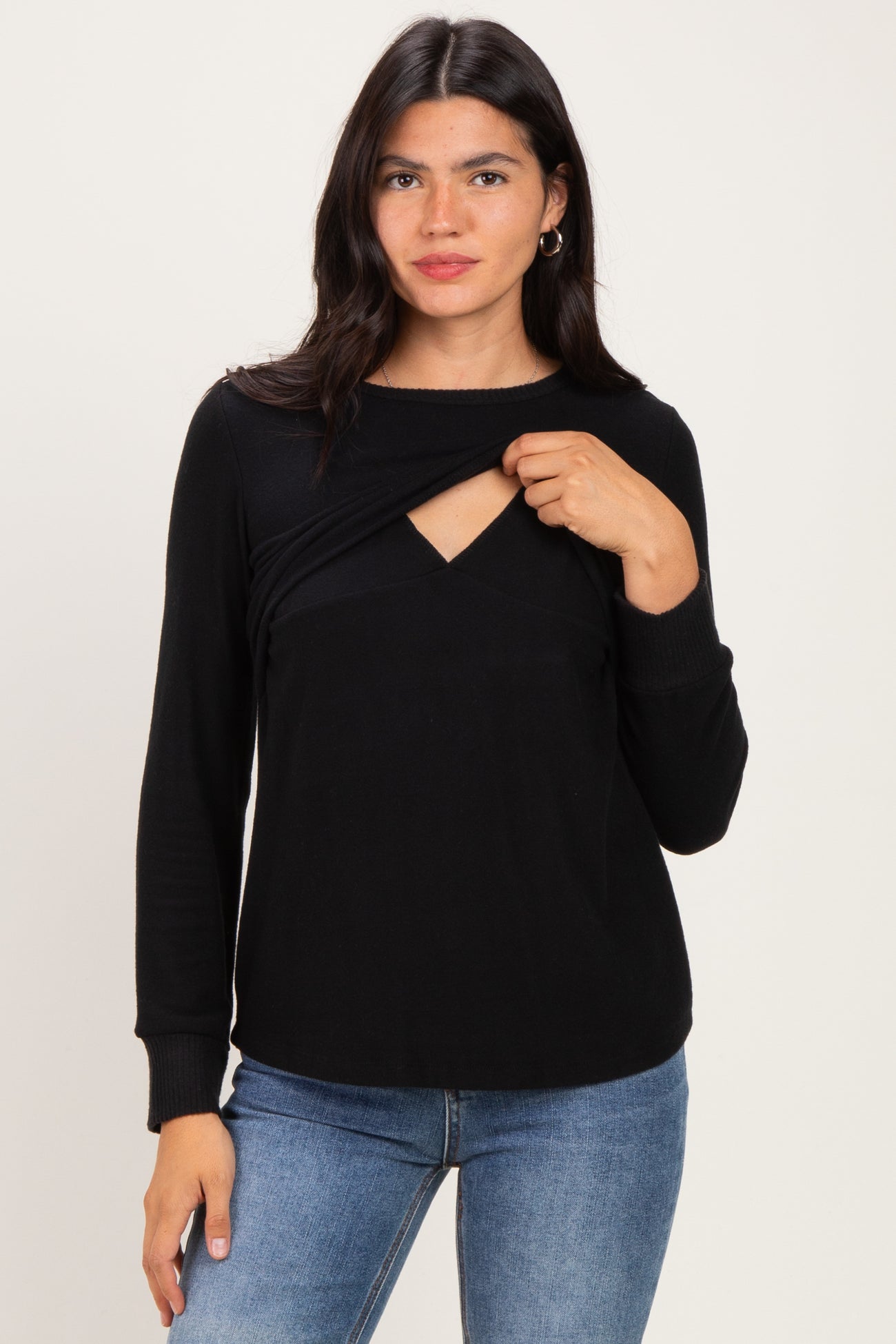woman wearing a black long sleeve top with a twist front detail and a cut-out neckline, styled with blue jeans