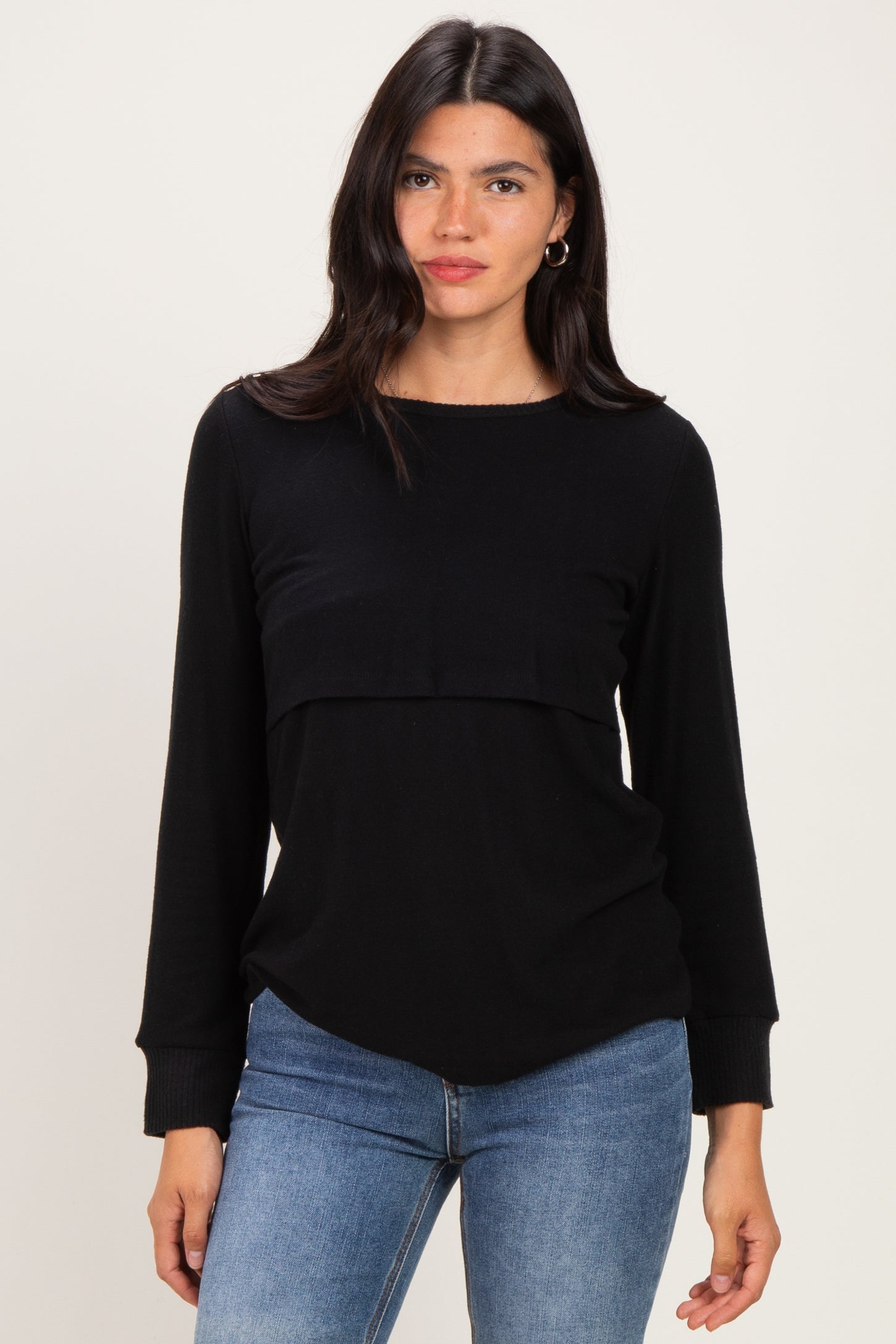 woman wearing a black long sleeve top with a layered design and relaxed fit, paired with blue jeans