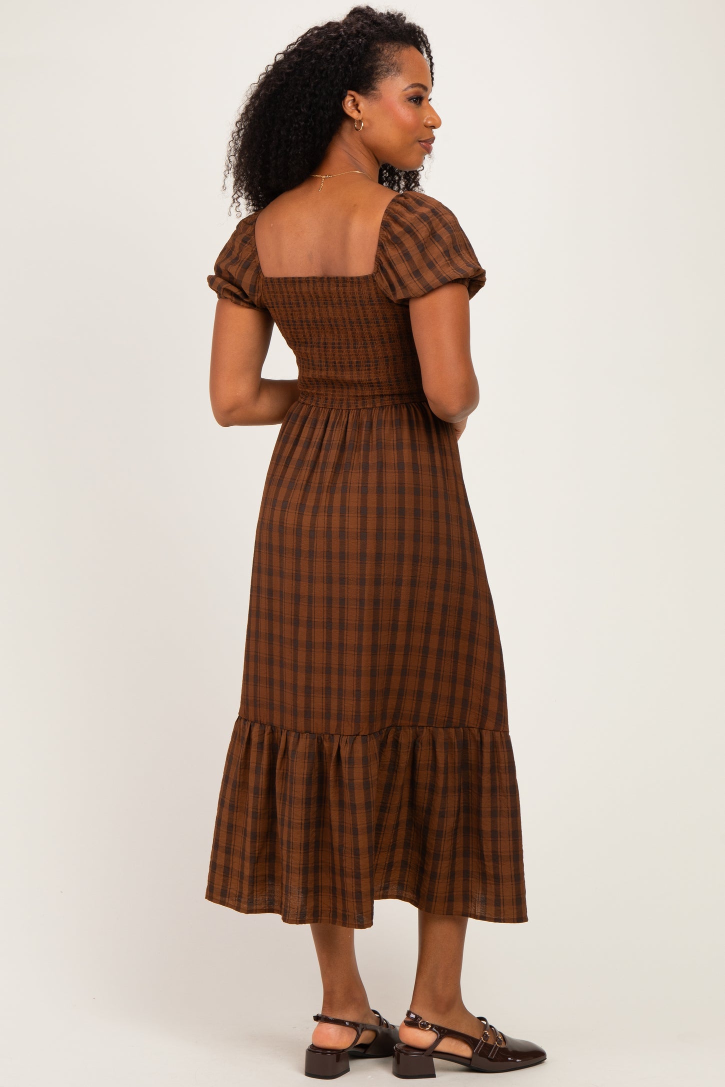 woman wearing a brown plaid puff sleeve midi dress with a smocked bodice and ruffled hem, viewed from the back