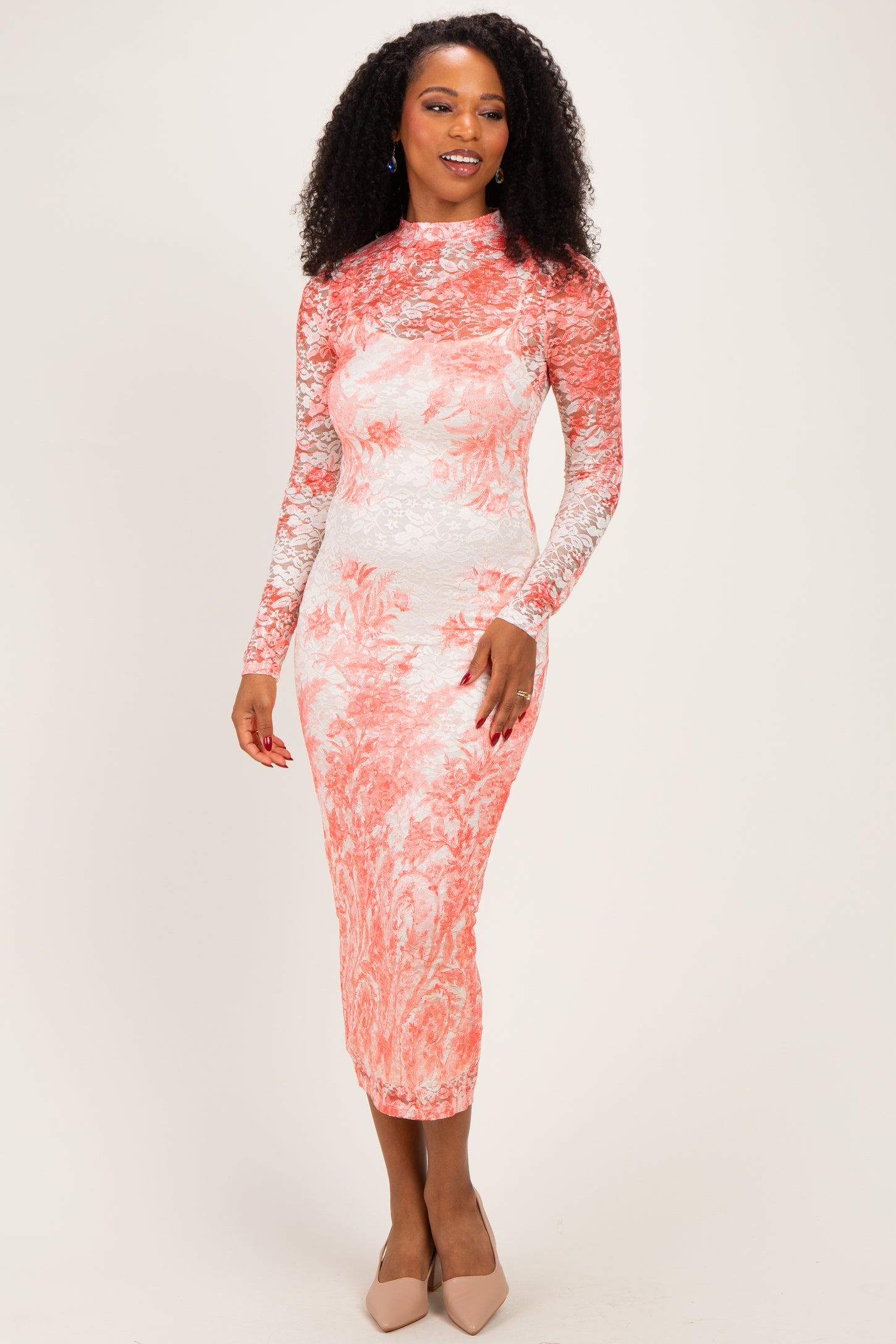 woman wearing a floral lace long sleeve bodycon dress in coral and white, standing and smiling