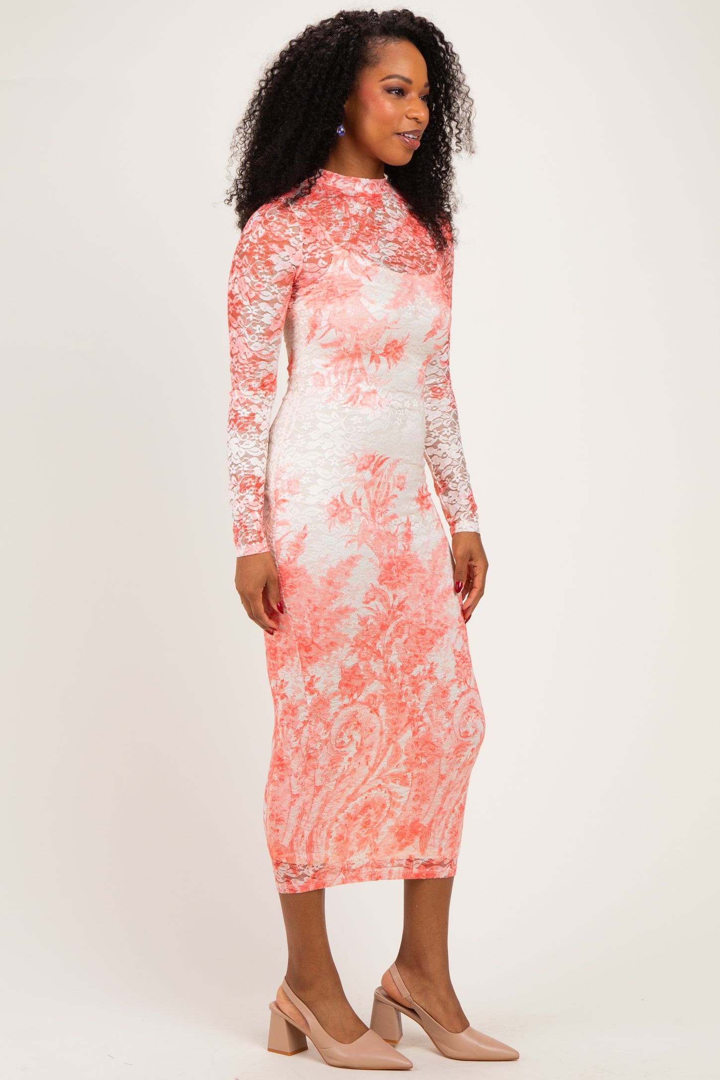 woman wearing a long sleeve, lace overlay midi dress in coral and white floral pattern with nude heels
