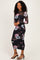 woman wearing a black floral long sleeve midi dress with sheer sleeves and fitted silhouette