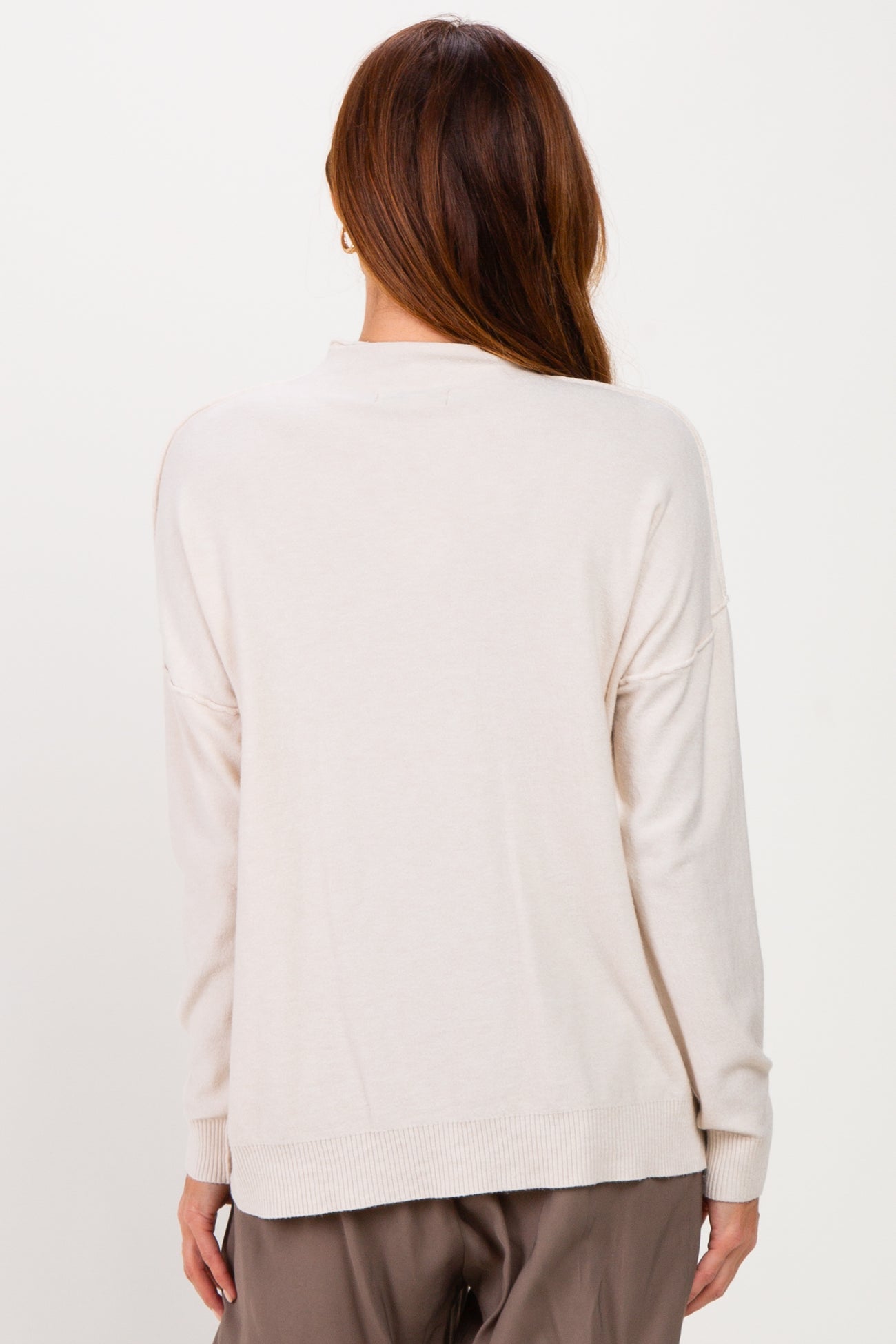 woman wearing a beige oversized sweater with long sleeves and a relaxed fit, viewed from the back