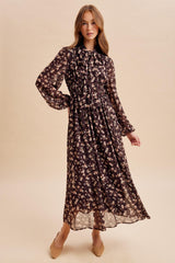 woman wearing a long sleeve black floral maxi dress with a cinched waist and ruffled collar, posing against a light background