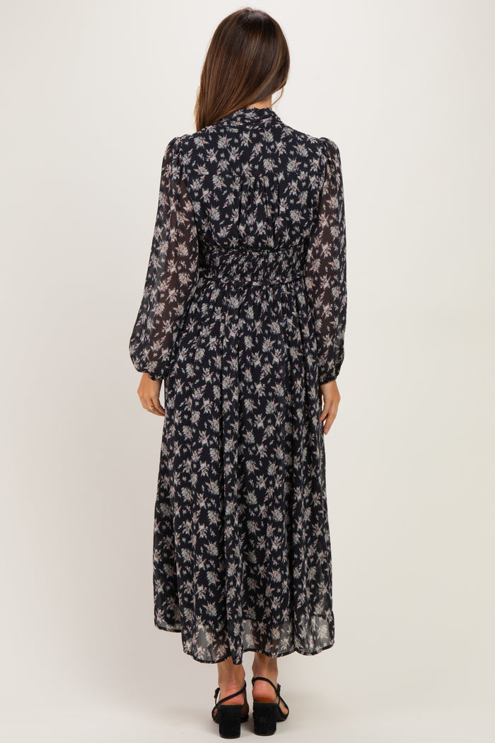 woman wearing a black floral maternity dress with long sleeves and a cinched waist, standing from the back
