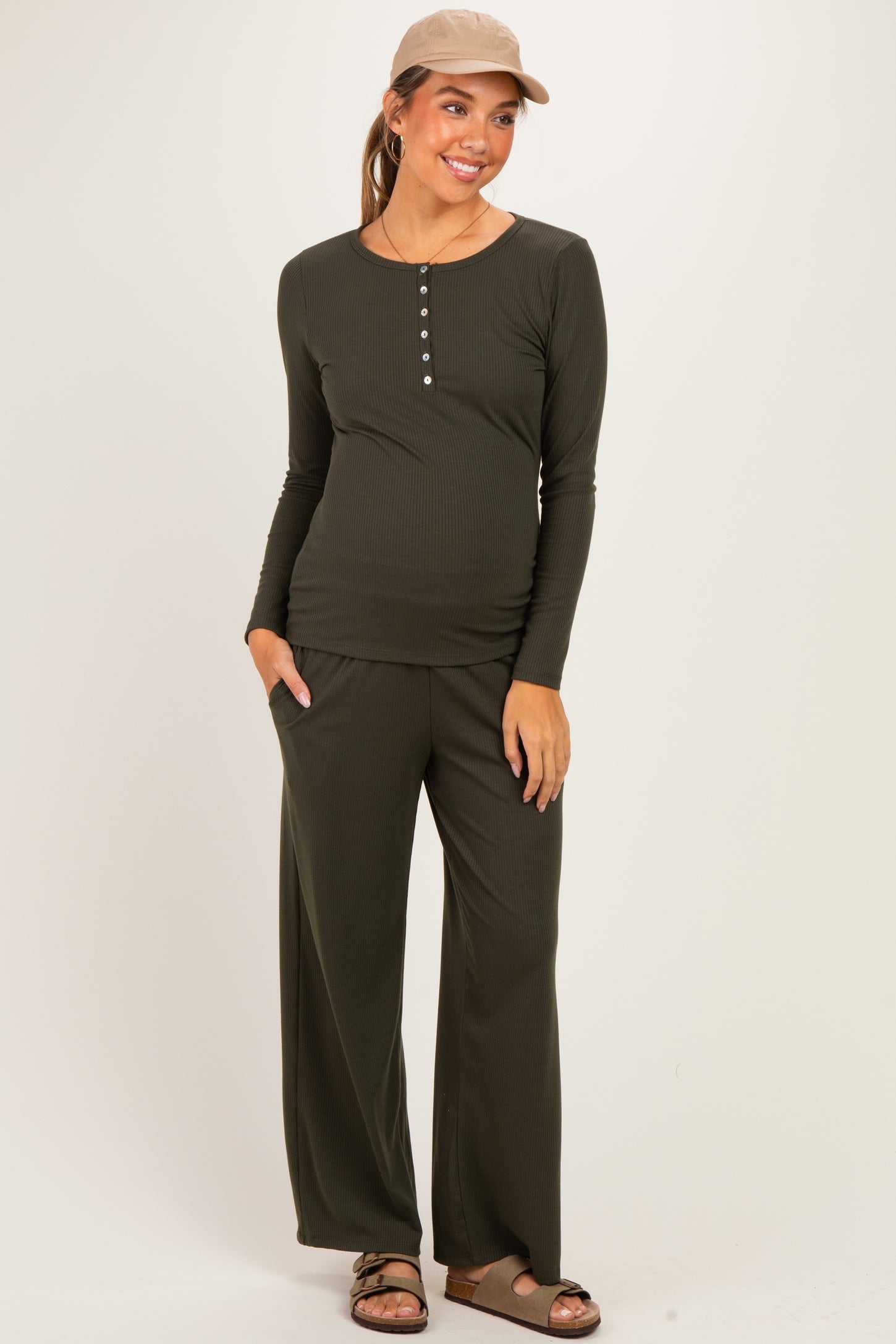 woman wearing a dark green long sleeve maternity top and matching pants, showcasing her baby bump