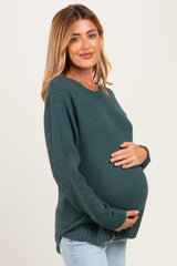 woman wearing a dark green knitted maternity sweater and holding her baby bump