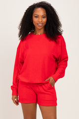 woman wearing a bright red oversized sweatshirt and matching shorts, smiling at the camera