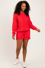 woman wearing a bright red long sleeve sweatshirt and matching shorts, styled casually with white sneakers