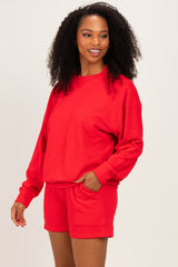 woman wearing a red oversized sweatshirt and matching red shorts, standing and smiling