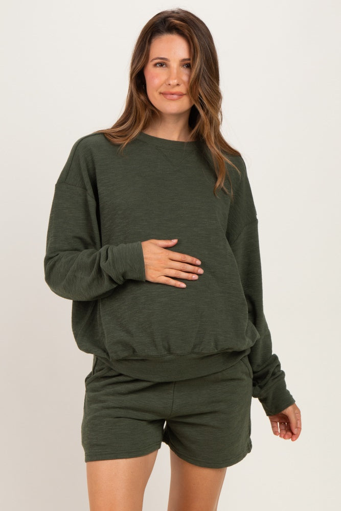 woman wearing a dark green maternity sweatshirt and matching shorts, holding her baby bump